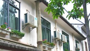 Un edificio con múltiples unidades de aire acondicionado, plantas en macetas en los alféizares de las ventanas y un estilo arquitectónico tradicional.