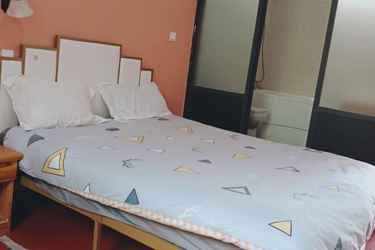 Una cama con una colcha estampada, un cabecero de madera y almohadas blancas.
