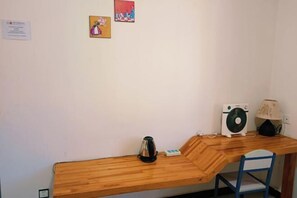 A small wooden desk with a kettle, a fan, and a lamp.