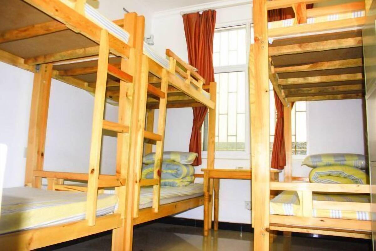 Una habitación con tres literas, una ventana con cortinas y una mesita pequeña.