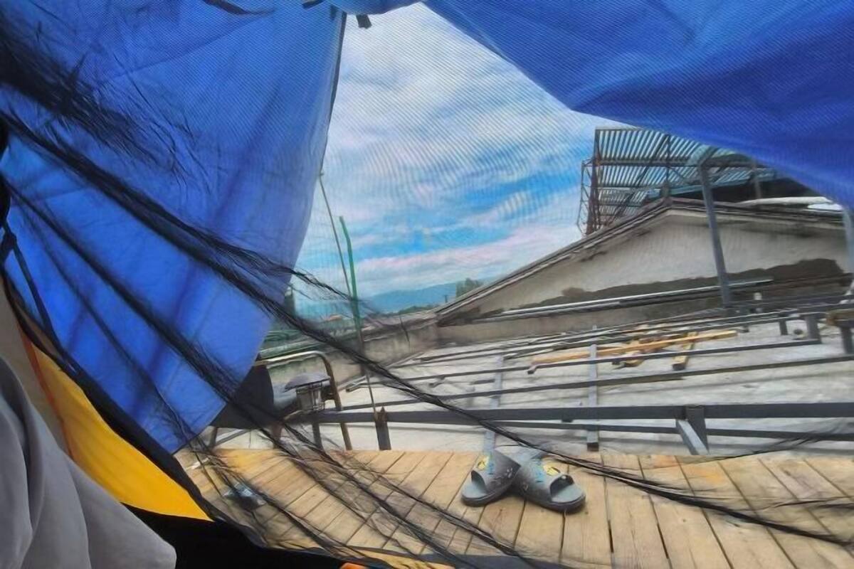 Una azotea con una lona azul, barandillas metálicas y materiales de construcción dispersos.