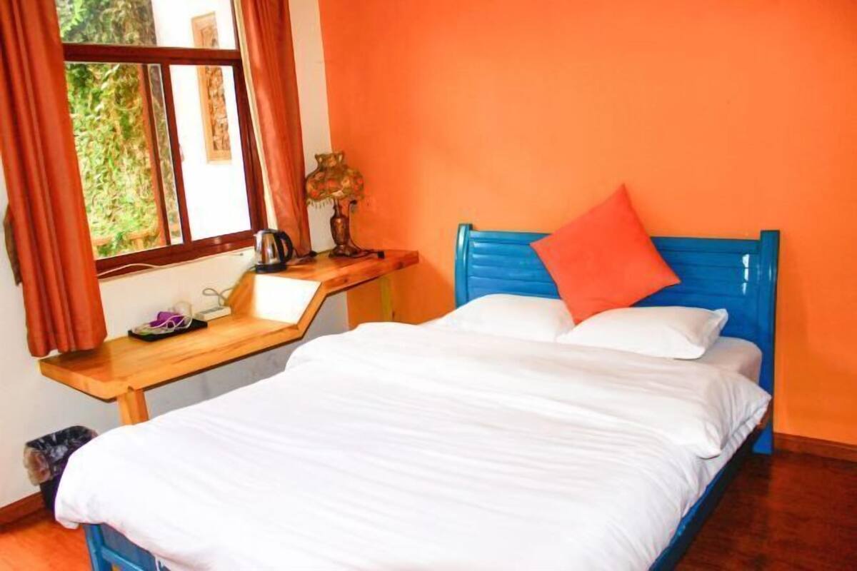Un dormitorio con cama, un escritorio de madera, una lámpara y una ventana con cortinas.