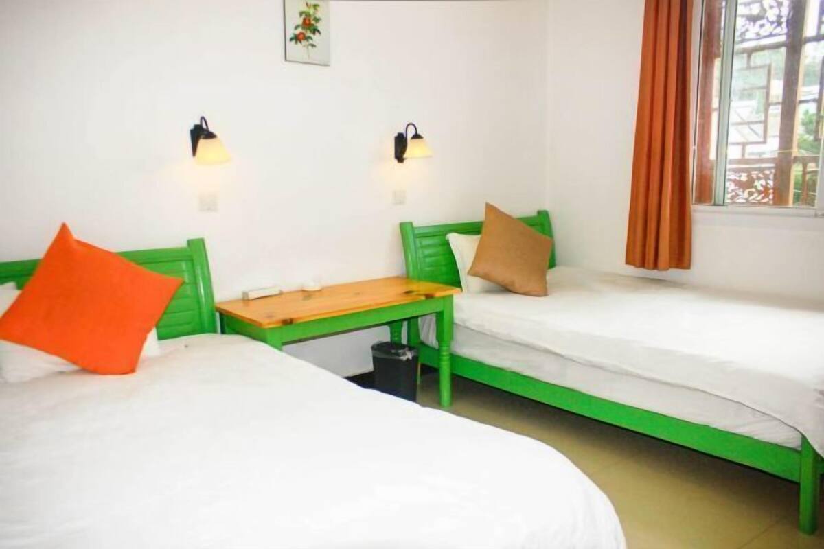 Una habitación con dos camas verdes, ropa de cama blanca, una mesa de madera y dos luces fijadas a la pared.