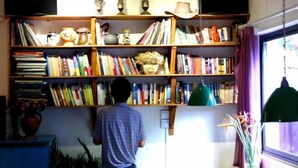 Una habitación con una estantería llena de libros, un escritorio con un ordenador y una ventana con cortinas.