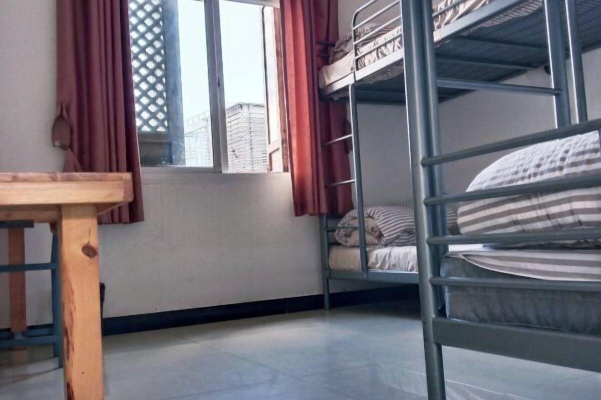Un dormitorio con literas, una mesa de madera y un ventanal con cortinas.
