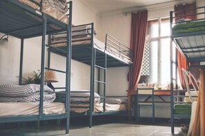 A dormitory room with bunk beds, a desk, and a window with curtains.