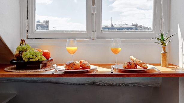 Ontbijt met croissants, fruit en sap op een tafel bij een raam met uitzicht op de stad.