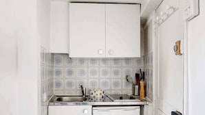 Een kleine keuken met een wit kastje, een decoratieve spatwand en een kleine koelkast.