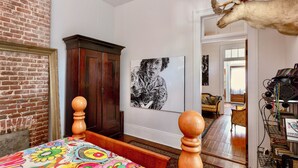 Une chambre avec un mur en briques, un lit en bois, un grand tableau, une armoire et une décoration représentant une tête de cerf.