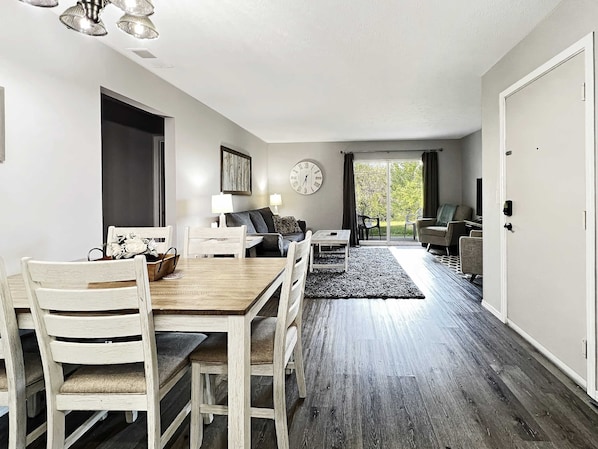 A modern living room with a dining area, a sofa, a TV, and a view of the outdoors.