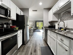 A modern kitchen with stainless steel appliances, white cabinetry, and a dining area with a view.