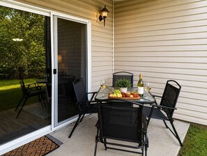 Un patio exterior con una mesa lista para dos personas, que incluye una botella de vino, copas y una bandeja de fruta.
