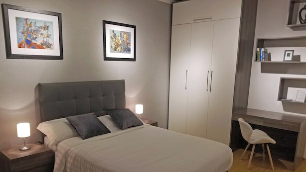Ein Schlafzimmer mit einem Bett, Nachttischen, einem Schreibtisch und einem Sessel. An der Wand hängen zwei gerahmte Bilder.