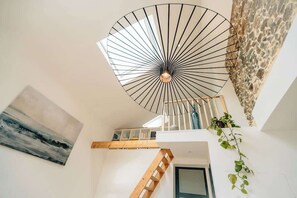 Stunning interior space with a unique ceiling fan and a wooden staircase leading to an upper level, featuring a beautiful painting and a potted plant.