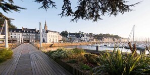 Stroll along the waterfront boardwalk, lined with lush greenery, towards the marina and historic buildings.