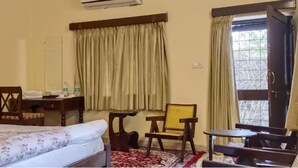 Habitación de hotel con cama, escritorio, silla, una mesita y ventana con cortinas.