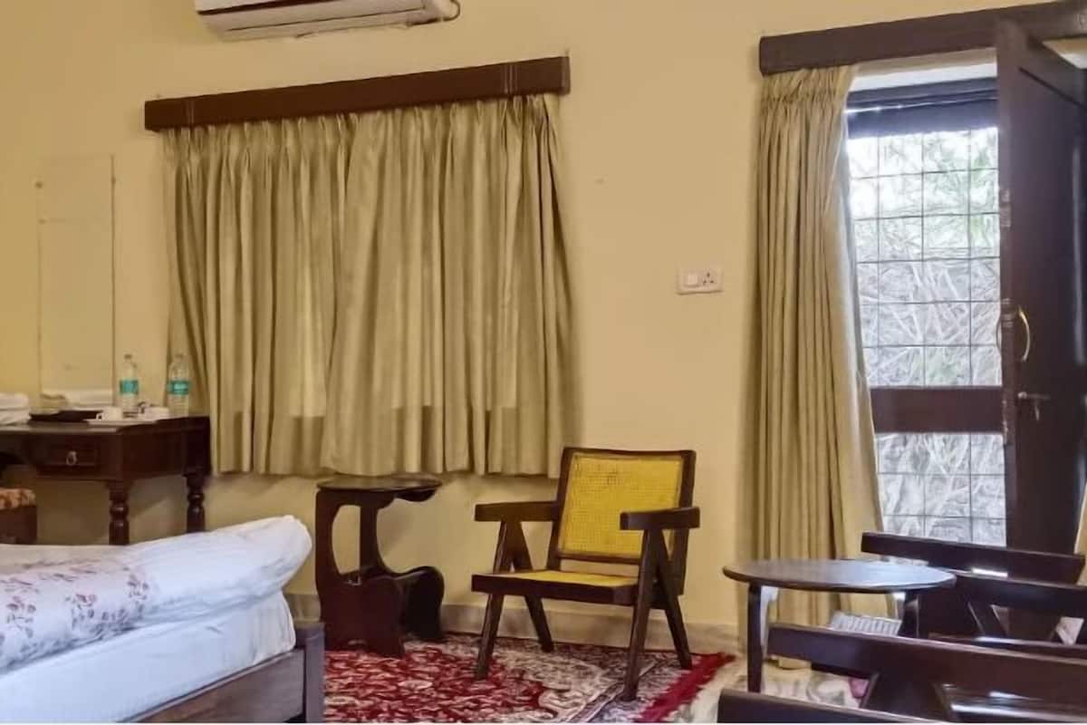 Habitación de hotel con cama, escritorio, silla, una mesita y ventana con cortinas.