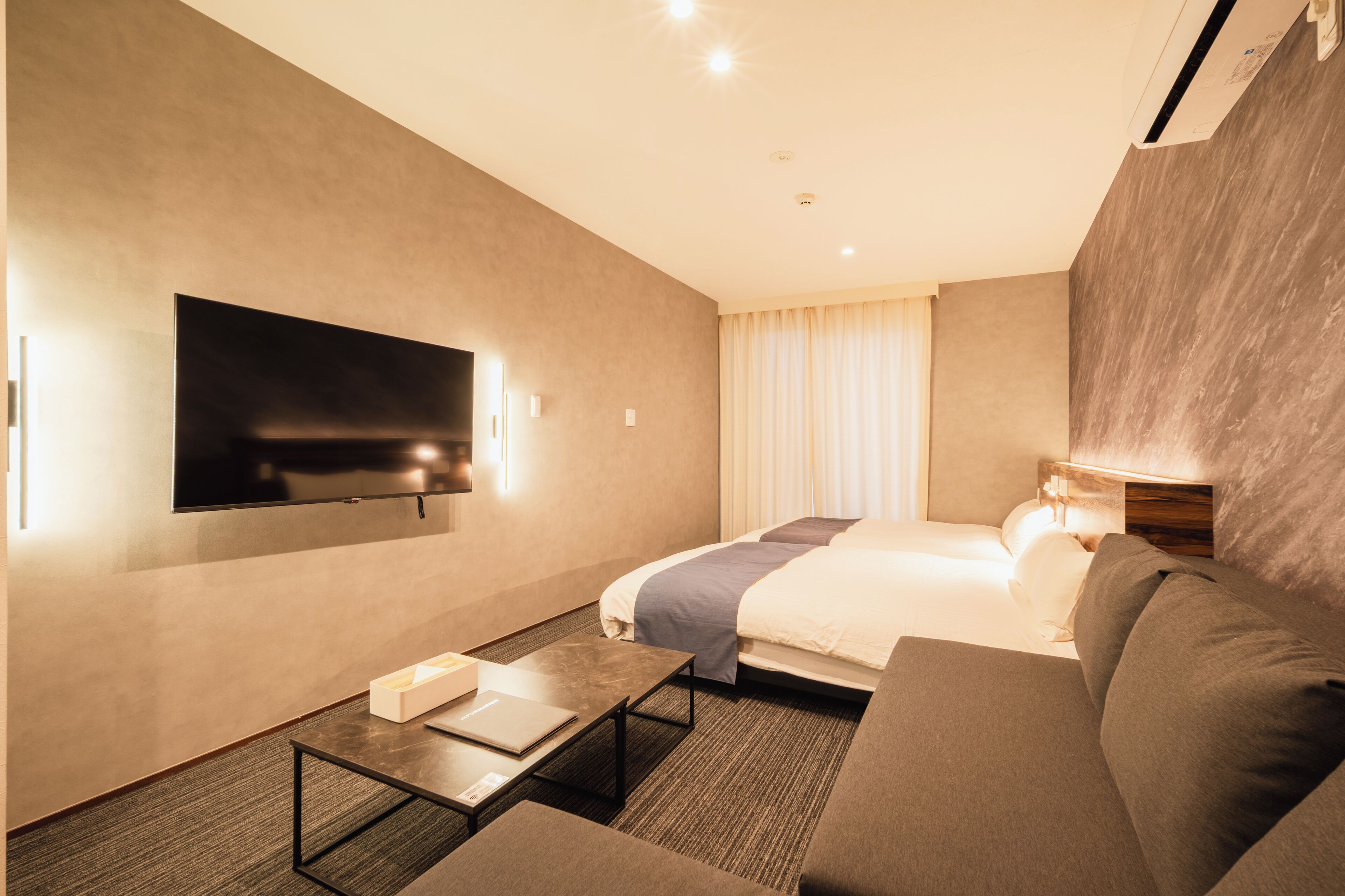 A hotel room with a bed, a TV mounted on the wall, a sofa, and a table.
