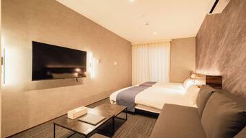 A hotel room with a bed, a TV mounted on the wall, a sofa, and a table.