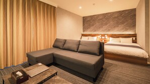 Une chambre d’hôtel moderne avec un canapé d’angle, un lit doté d’une tête de lit en bois et une petite table avec un coffre.