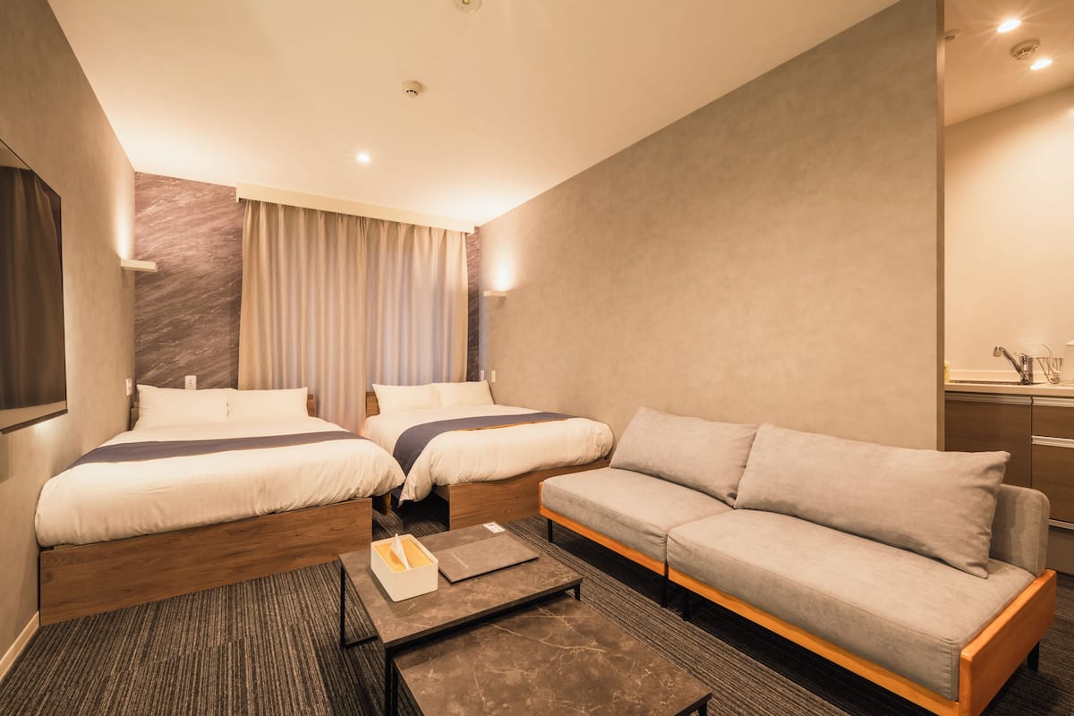 Une chambre d’hôtel avec deux lits, un canapé, une petite table et un miroir.