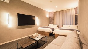Une chambre d’hôtel avec deux lits, un téléviseur à écran plat fixé au mur, une petite table et un canapé.