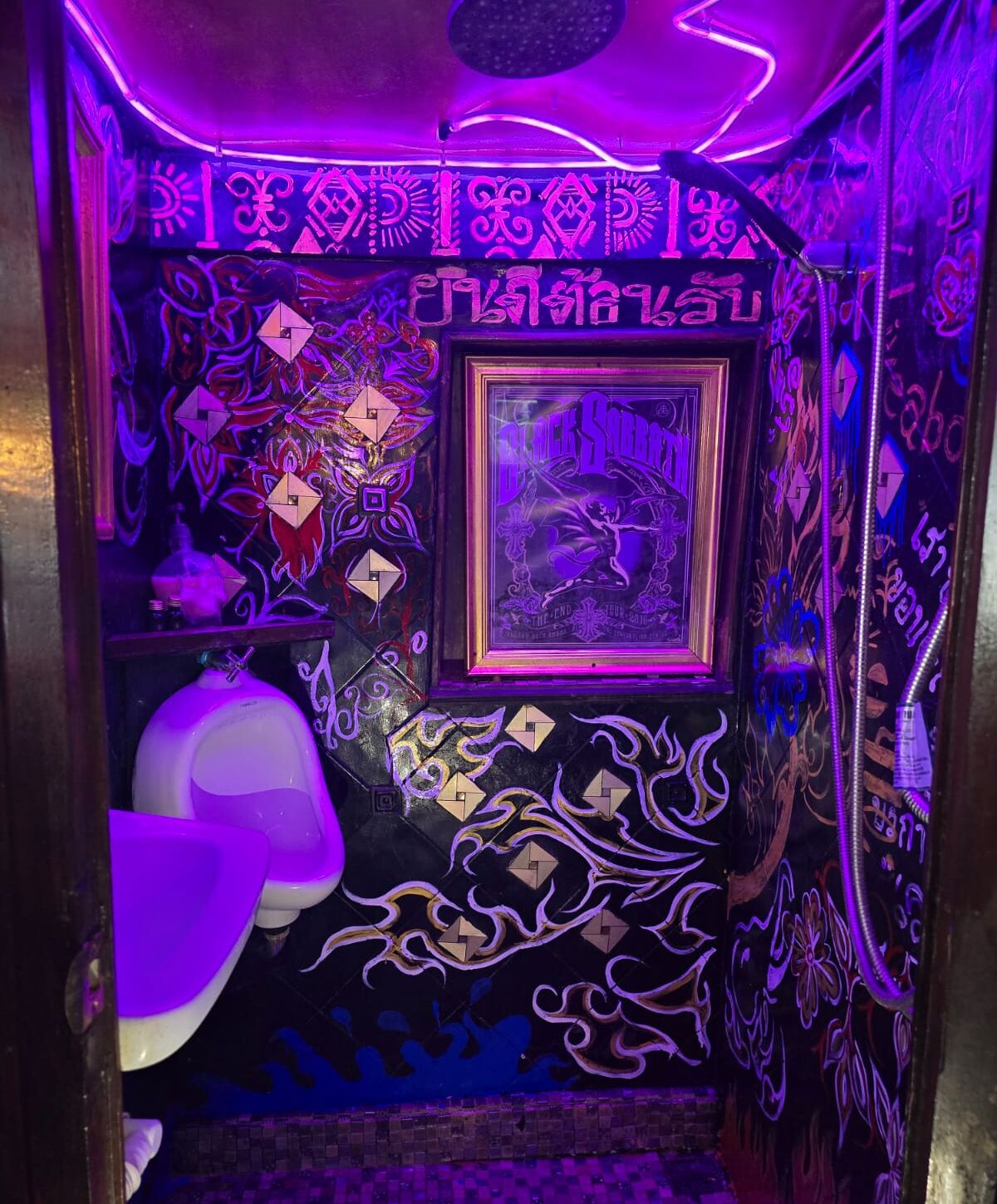 A bathroom with intricate wall designs, a framed poster, and a white urinal.
