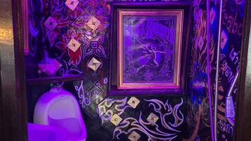 A bathroom with intricate wall designs, a framed poster, and a white urinal.