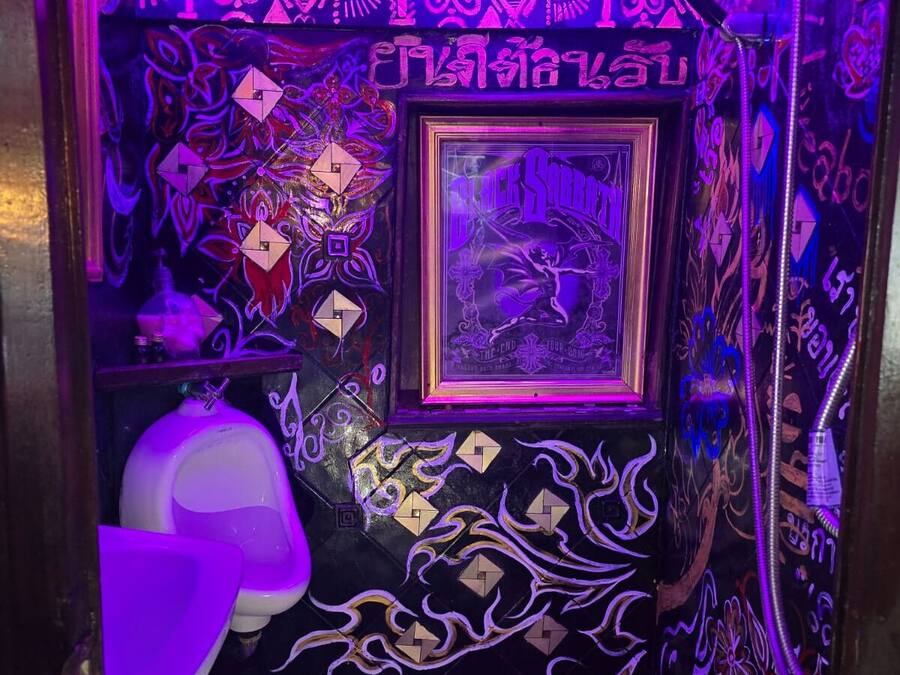 A bathroom with intricate wall designs, a framed poster, and a white urinal.