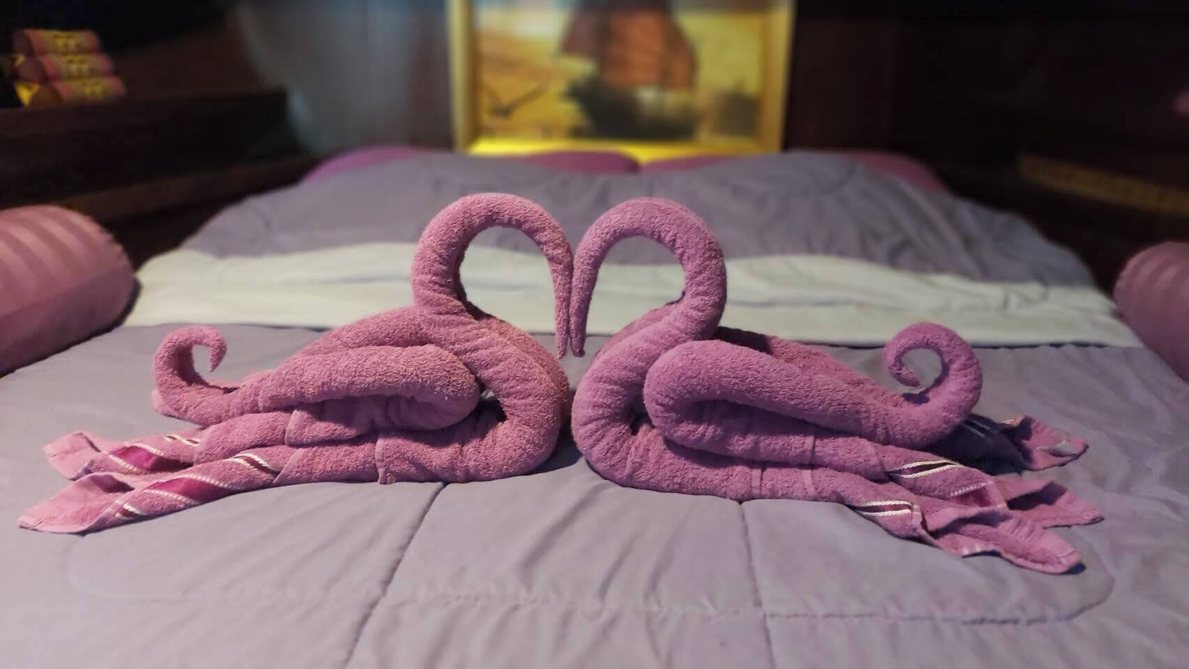 A bed with a purple blanket and two towels arranged in the shape of swans.