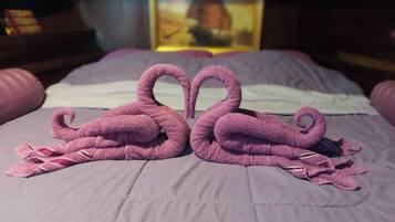 A bed with a purple blanket and two towels arranged in the shape of swans.