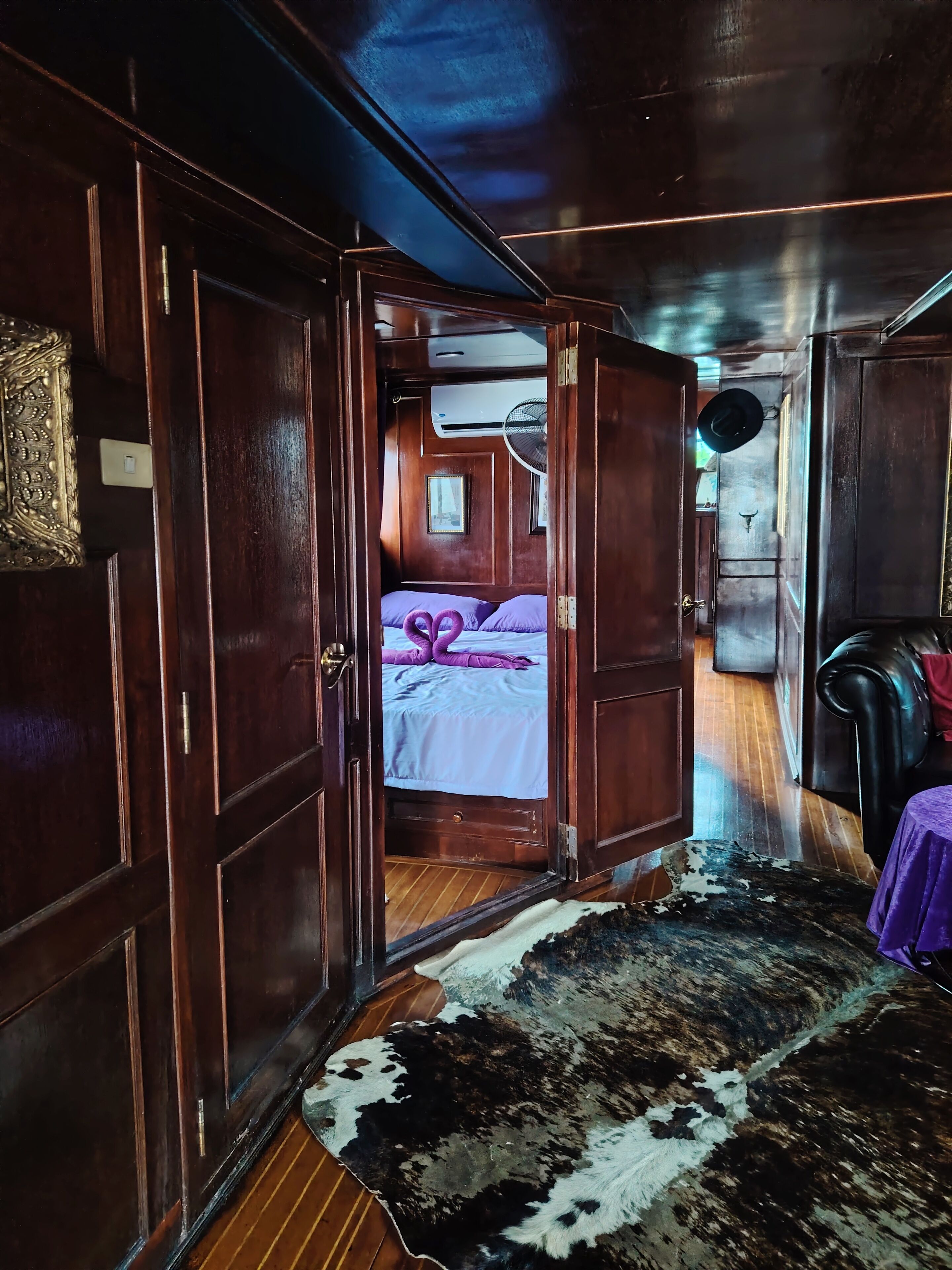 Een kamer met een bed, houten wanden, een plafondventilator en een koeienhuidtapijt.