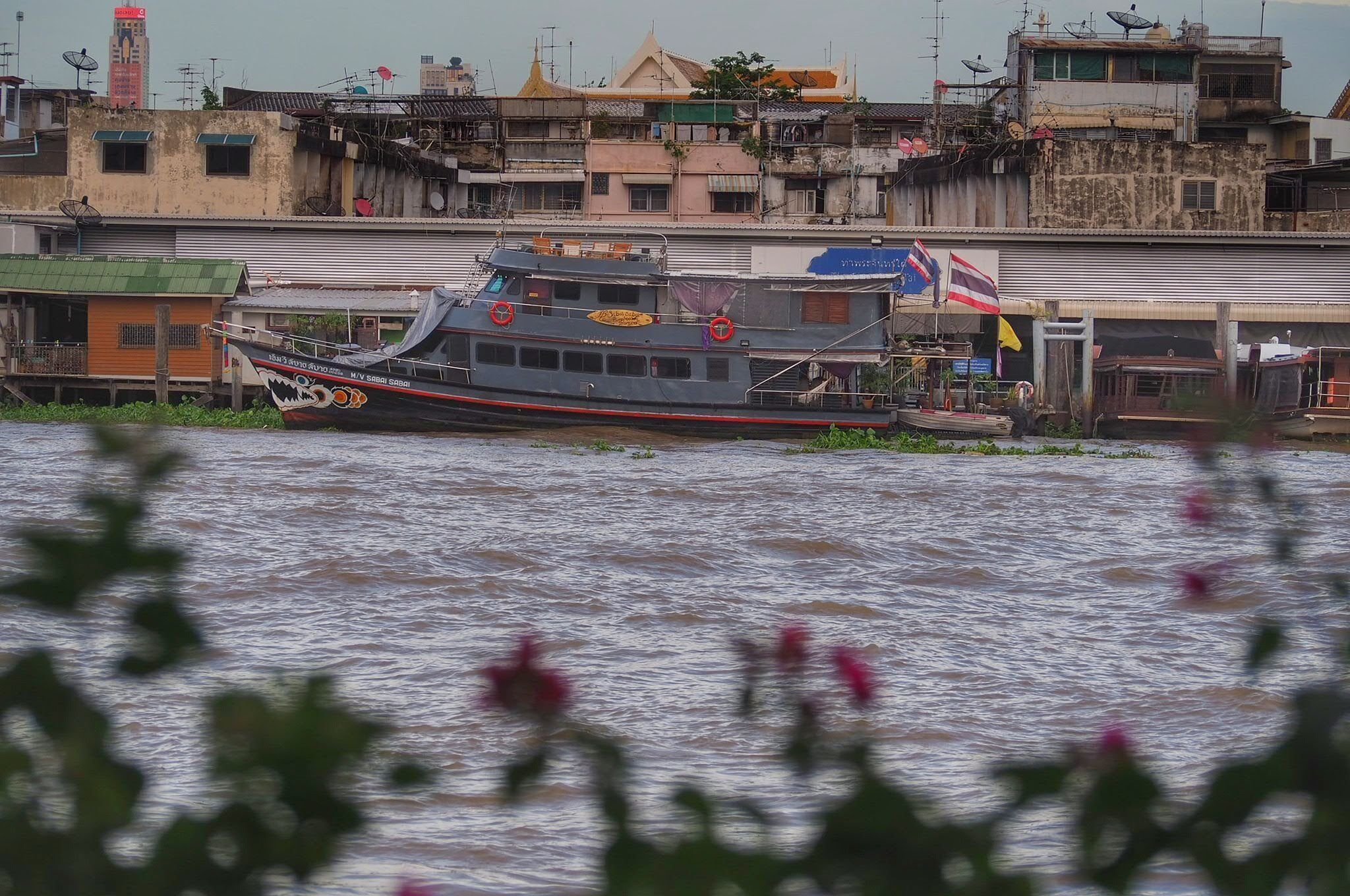 A boat docked at a riverside location with buildings in the background.