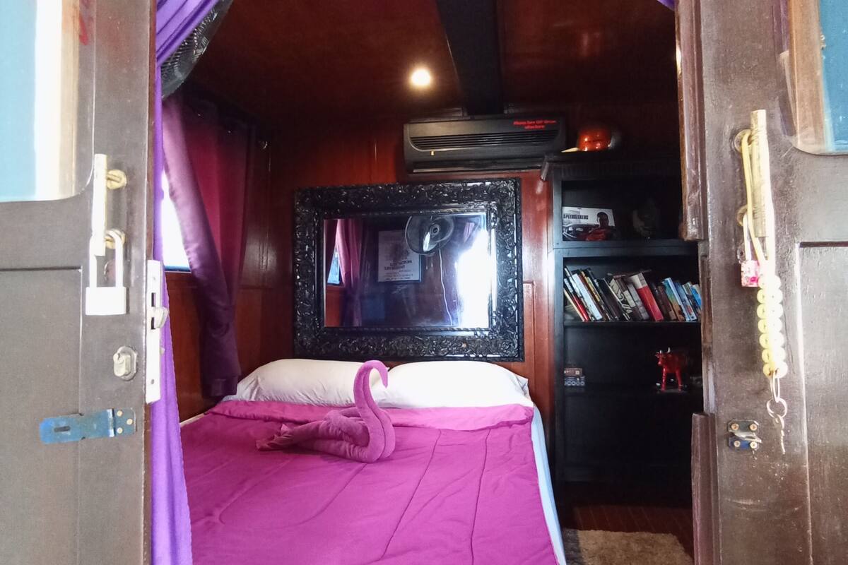 Quarto com cama, cortinas roxas, um espelho e uma estante.