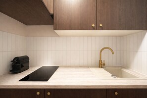A kitchen with a black induction cooktop, a gold faucet sink, and wooden cabinets. - TOCQUEVILLE (Paris)