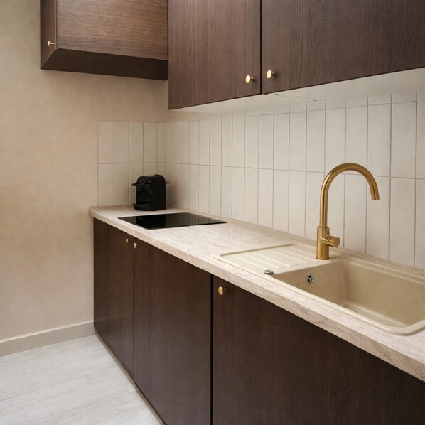 A kitchen with dark wooden cabinets, a white tiled backsplash, a black coffee maker, and a gold faucet. - TOCQUEVILLE (Paris)