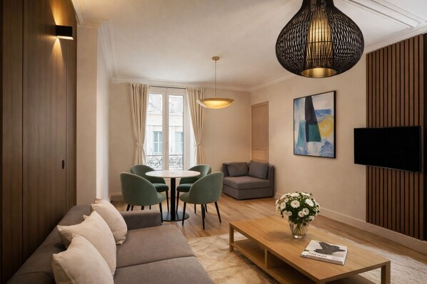 Un salon moderne comprenant un canapé, une table à manger avec des chaises, une table basse, un téléviseur et un grand luminaire suspendu.