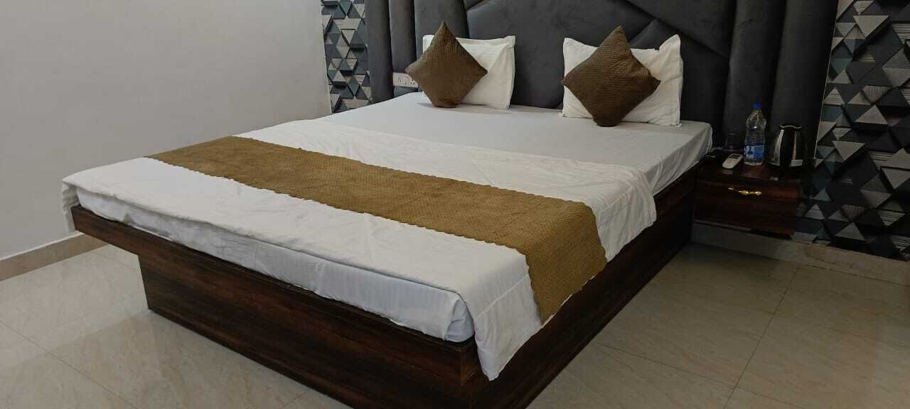 Ein ordentlich bezogenes Bett mit einer braunen Decke und weißen Bettwäsche, ein dunkles Holz-Kopfteil und eine Wand im Hintergrund mit einem geometrischen Muster.