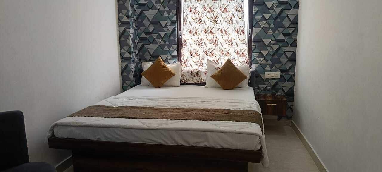 A bedroom with a bed, two pillows, a window with patterned curtains, and a geometric wall design.