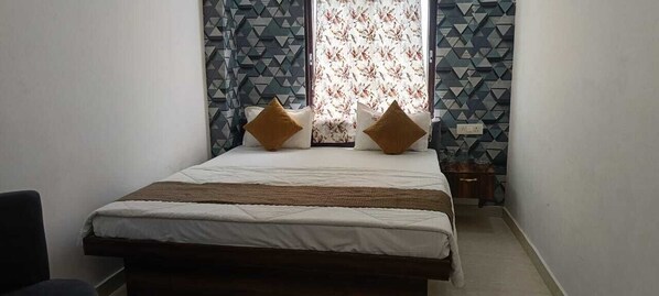 A bedroom with a bed, two pillows, a window with patterned curtains, and a geometric wall design. - SHEHNAI RESORT Hotel &Restaurant (Supaul)