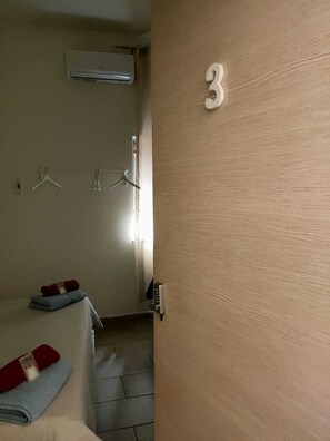 Una habitación con una cama, aire acondicionado de pared, una puerta con el número 3 y un perchero con ganchos.