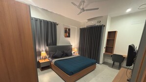 Una camera da letto con un letto, comodini, una scrivania, una sedia, una ventola a soffitto e una TV.