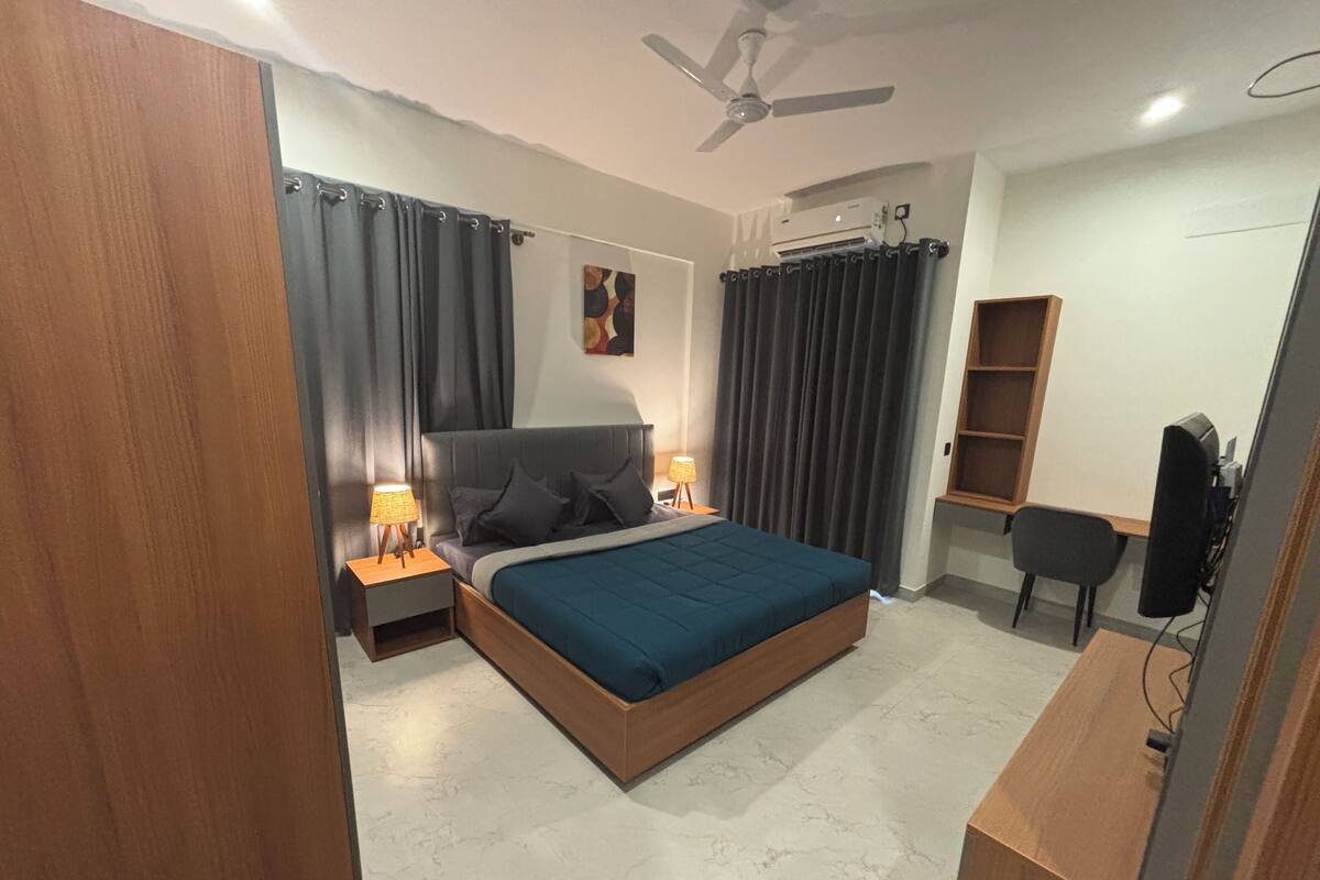 Une chambre à coucher comprenant un lit, des tables de chevet, un bureau, une chaise, un ventilateur de plafond et un téléviseur.