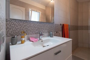 A bathroom with a white sink, a mirror, a shower area, and a tiled backsplash.