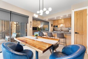 A modern kitchen with wooden cabinets, a built-in microwave, and a dining area with a wooden table and blue leather chairs.