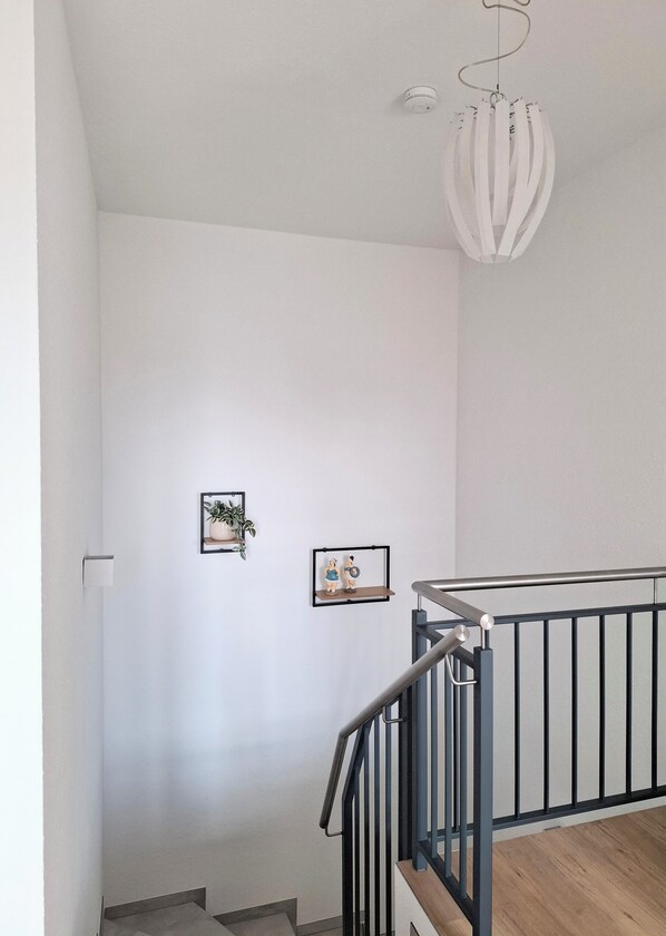 Una escala amb barana metàl·lica, paret blanca i un llum penjant.