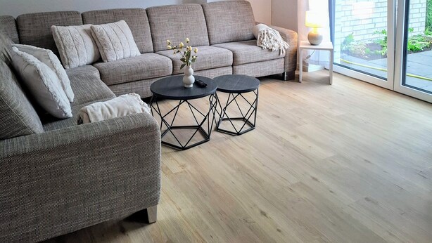 A modern living room with a grey sofa, two round coffee tables, and a large window with a view of greenery. - Vacation home Wolke7, with garden, 250 meters to the lake (Lembruch)