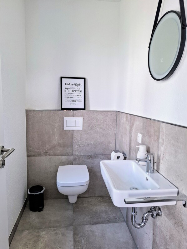 A modern bathroom with a toilet, sink, and a framed quote on the wall.