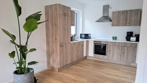A modern kitchen with wooden cabinets, a built-in oven, and a microwave. - Vacation home Wolke7, with garden, 250 meters to the lake (Lembruch)