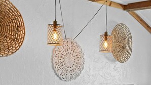A bedroom with a wooden ceiling, two hanging woven light fixtures, a decorative wall piece, and a bedside table with a phone.
